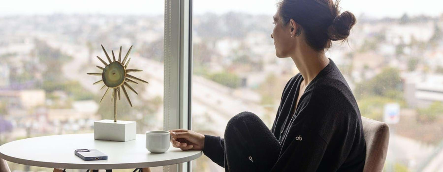 A resident sitting at a table having coffee at Ancora Apartments in Little Italy, San Diego, featuring a view of the city.