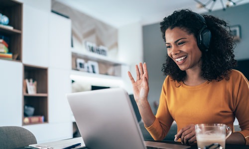 a woman smiling and waving at a computer
